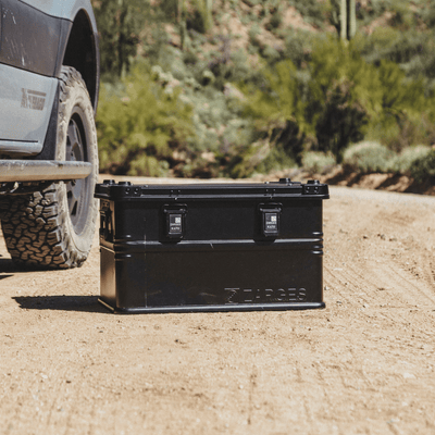 ZARGES K470-Matte Black-31013205 case on a desert dirt road beside an off-road truck's tire
