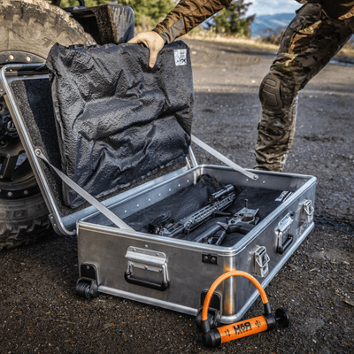 Hunter opens a wheeled ZARGES case beside a truck tire, KOR Takedown Kit panels over a broken-down rifle