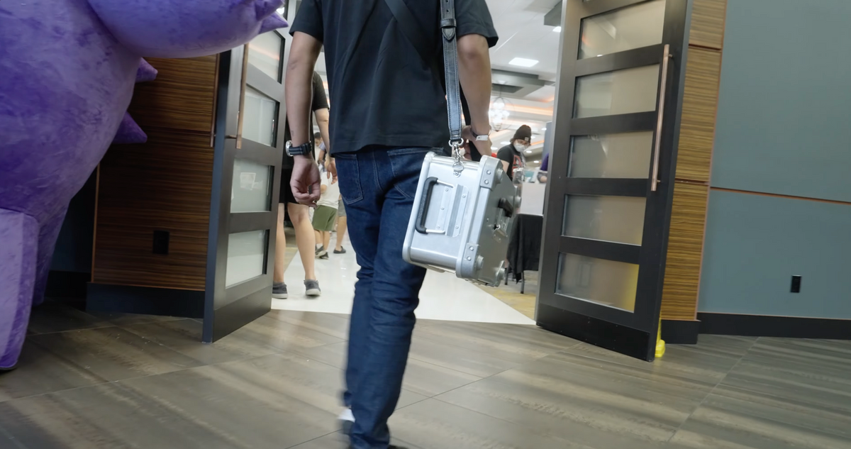 Man walking through an indoor venue with a small aluminum case slung on the ZARGES Leather Shoulder Strap