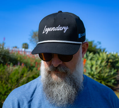 Bearded man in sunglasses wearing the ZARGES Legendary Black Rope Hat, front view under a blue sky