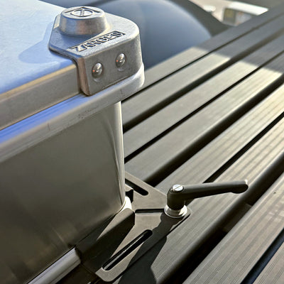 ZARGES mounting bracket clamped to a roof rack slat, holding an aluminium case
