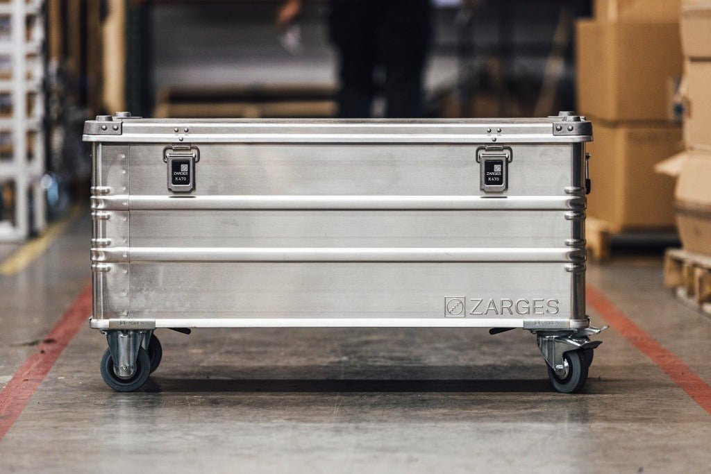 ZARGES Casters (set of two) fitted under an aluminum case on a warehouse floor, side view